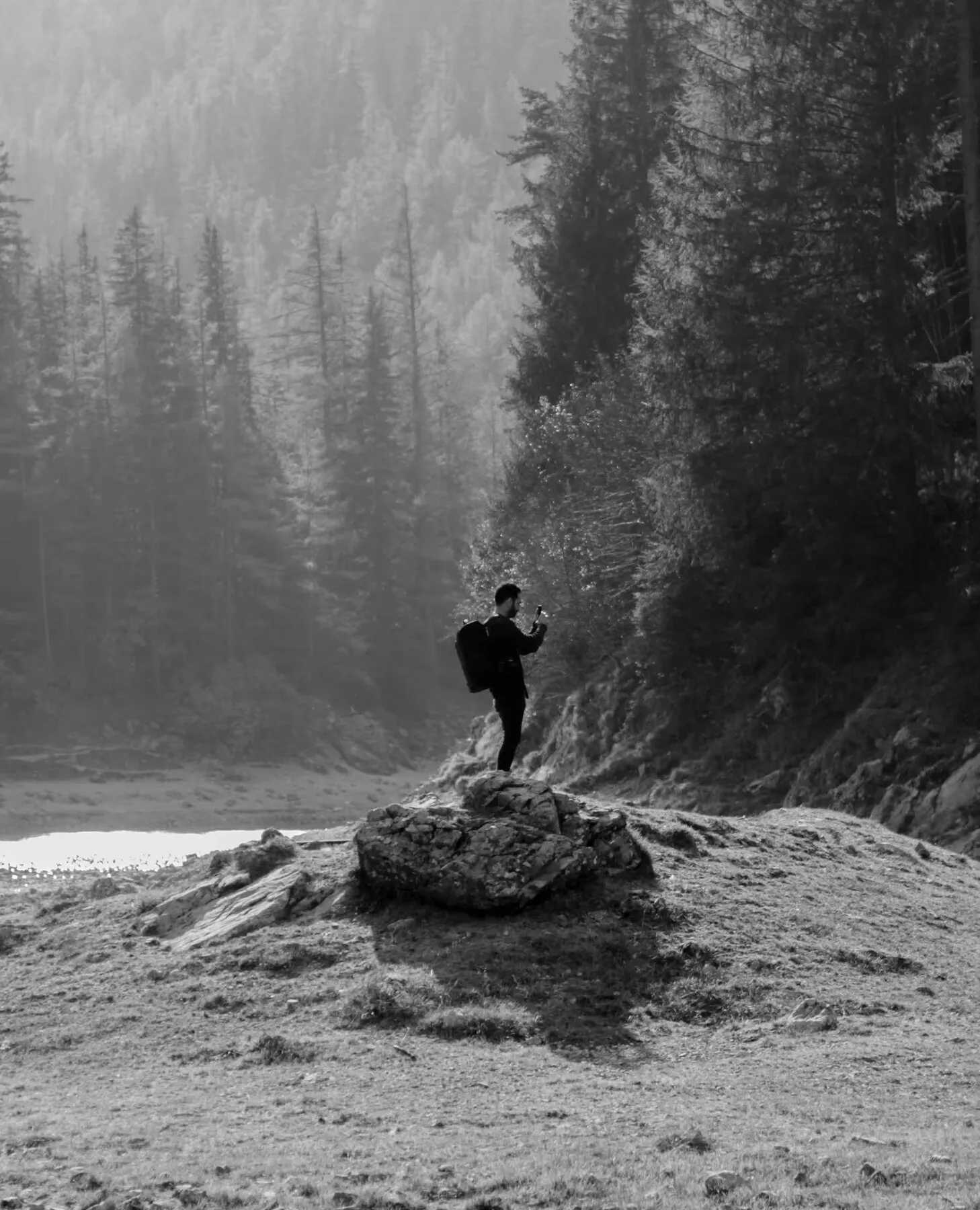 Rock standing on a rock by a mountain lake, in black and white